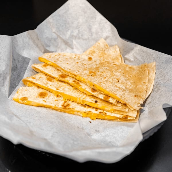 Four cheesy quesadilla slices, golden brown and filled with melted cheese, served in a paper-lined basket.