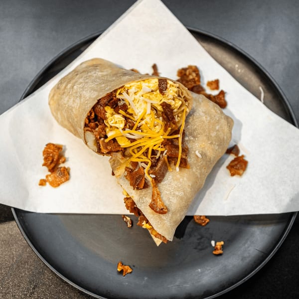 A large breakfast burrito, cut in half, filled with eggs, cheese, and chorizo on a black plate.