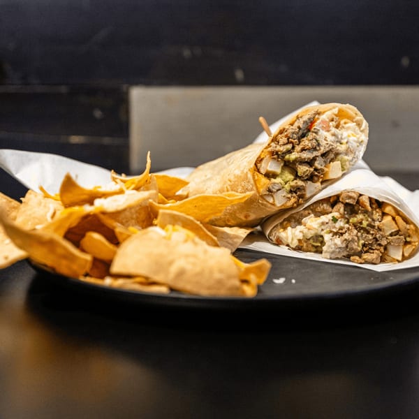 Two carne asada burritos with guacamole and cheese, served with a side of tortilla chips.