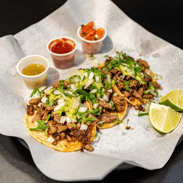 Two El Burrito Taco Shop carne asada tacos with cilantro, onions, guacamole, and lime wedges.